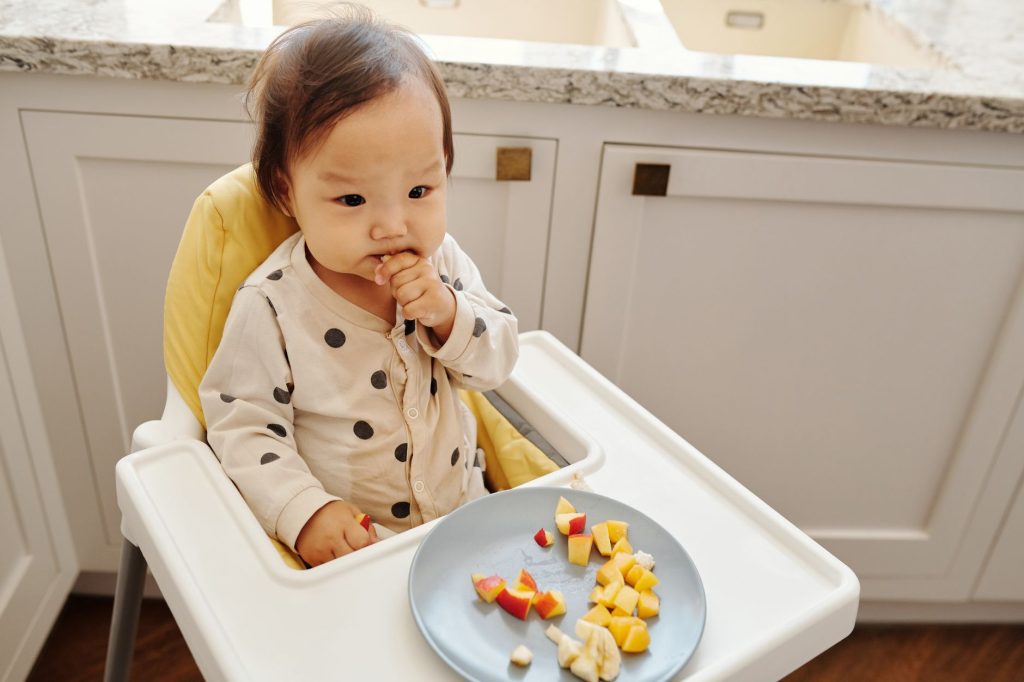 Bébé attablé qui attrape des morceaux d'aliments avec ses doigts en diversification menée par l'enfant